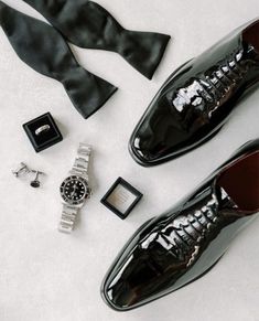 a pair of black shoes, tie and watch on a white surface with other accessories