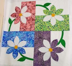 four squares with flowers on them in different colors and sizes, each one being quilted