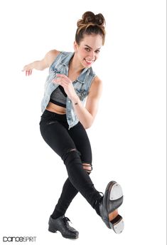 a woman in black pants and a denim vest is doing a trick with her skateboard