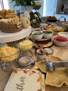 an assortment of cheeses and other food items on a kitchen counter with plates, bowls and utensils