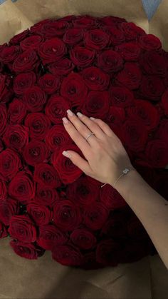 a woman's hand on top of a large bouquet of red roses in brown paper