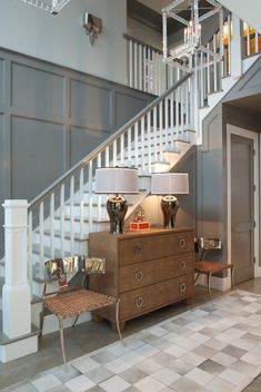 a living room with two lamps and a dresser in front of a stair case on the wall