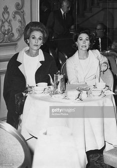 two women sitting at a table with tea cups and saucers on it in front of them