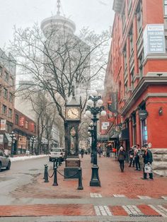 a clock on a pole in the middle of a city street with people walking around