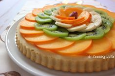 a fruit tart with sliced kiwi, oranges and bananas on top sits on a white plate