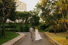 a bride and groom walking down the road in their wedding attire, with yellow leaves on the ground