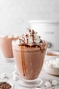 two glasses filled with hot chocolate and marshmallows on a white counter top