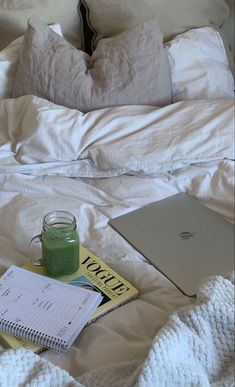 an open laptop computer sitting on top of a bed next to a cup of green liquid