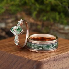 two wedding rings with green and white stones on top of each other sitting on a wooden surface