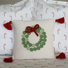 a white pillow with a red bow on it and a green beaded wreath in the middle