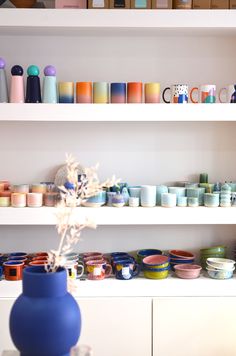 a blue vase sitting on top of a table next to shelves filled with cups and bowls