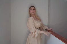 a woman in a beige dress leaning against a wall with her hand on the railing