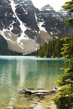 a lake surrounded by mountains with snow on the top and trees in the foreground