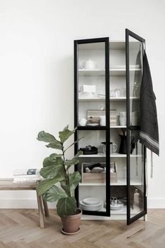 a black and white bookcase next to a potted plant on a wooden floor