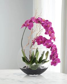 a glass vase filled with purple orchids on top of a white marble countertop