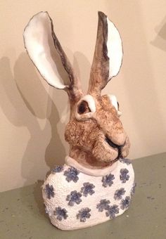 a statue of a rabbit with blue flowers on it's body and ears, sitting on a table