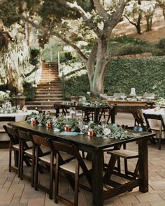 an outdoor dining area with wooden tables and white linens, greenery and candles