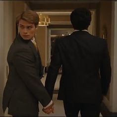 two people in suits walking down a hallway