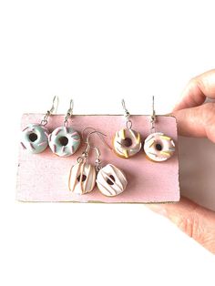 three pairs of donuts hanging from hooks on a pink board, with one being held up by a person's hand