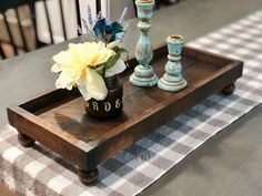 a wooden tray with vases and flowers on it sitting on a checkered table cloth