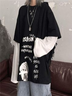 a woman standing in front of a brown couch wearing a black shirt with white writing on it