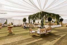 an outdoor event with tables, chairs and white draping on the ceiling is decorated with greenery