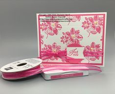 a pink ribbon is next to a card with flowers on it and a spool of thread