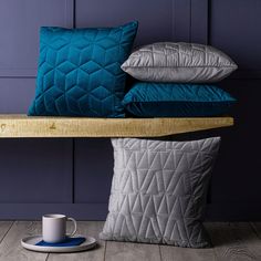 three pillows and a cup on a table with a blue wall in the back ground