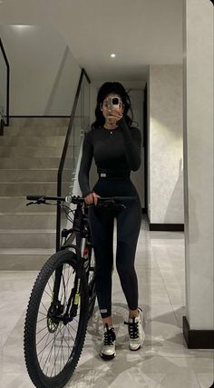 a woman taking a selfie while standing next to her bike in a hallway with stairs