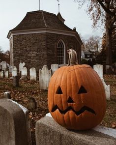 a carved pumpkin sitting on top of a stone wall in front of a cemetery with tombstones