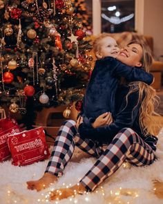 a woman holding a baby in front of a christmas tree