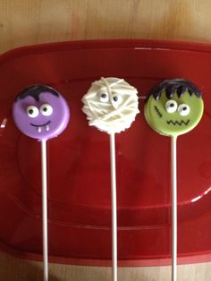 three lollipops with faces on them sitting on a red tray