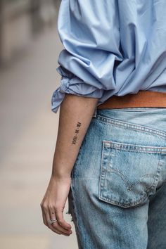 a woman with a small tattoo on her left arm, wearing jeans and a blue shirt