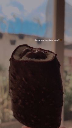 a person holding up a chocolate dessert in front of a window