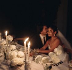 a bride and groom sitting at a table with candles