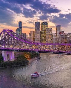 a boat traveling on the water in front of a bridge with purple lights and tall buildings