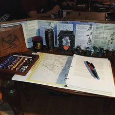 an open book sitting on top of a wooden table next to two pens and pencils