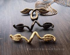 three decorative metal objects sitting on top of a wooden table next to leaves and wire