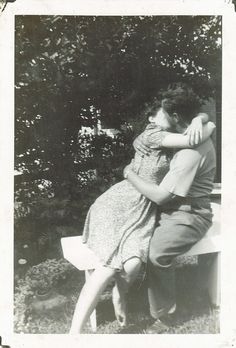 an old black and white photo of a man hugging a woman sitting on a bench