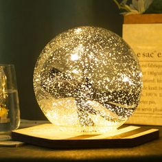 a snow globe sitting on top of a wooden table next to a glass filled with liquid