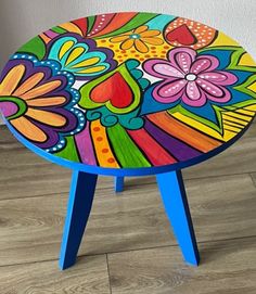 a brightly colored stool with flowers painted on the top and bottom, sitting on wood flooring