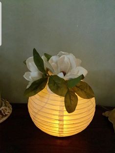 a white paper lantern with flowers in it sitting on a table next to a candle