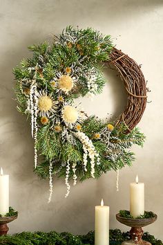 a wreath with white flowers and greenery is hung on the wall next to candles