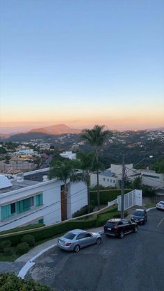 cars are parked in a parking lot next to some buildings and palm trees at sunset