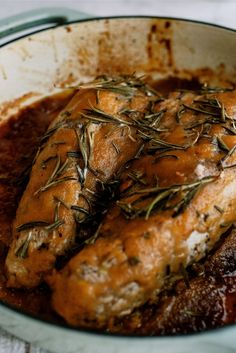 meat covered in gravy and garnished with fresh herbs on top, sitting in a pan