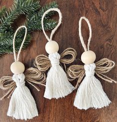 three white tasselled ornaments hanging from twine on a wooden table next to a christmas tree