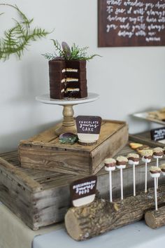 a table topped with cakes and cupcakes on top of wooden boxes next to trees