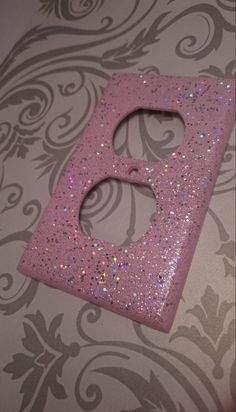 a pink glittered letter sitting on top of a wall next to a floral pattern