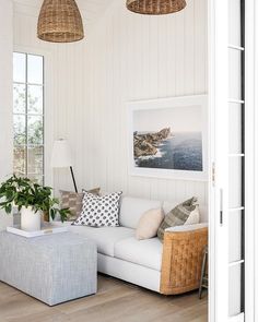 a living room with white walls and wood flooring, two wicker lamps hanging from the ceiling