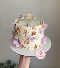 a hand holding a white cake with butterflies on it and a happy birthday topper